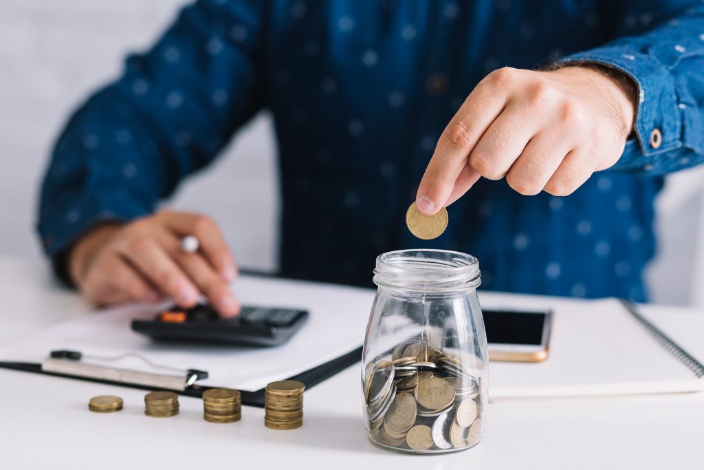 hand-putting-coin-jar-using-calculator